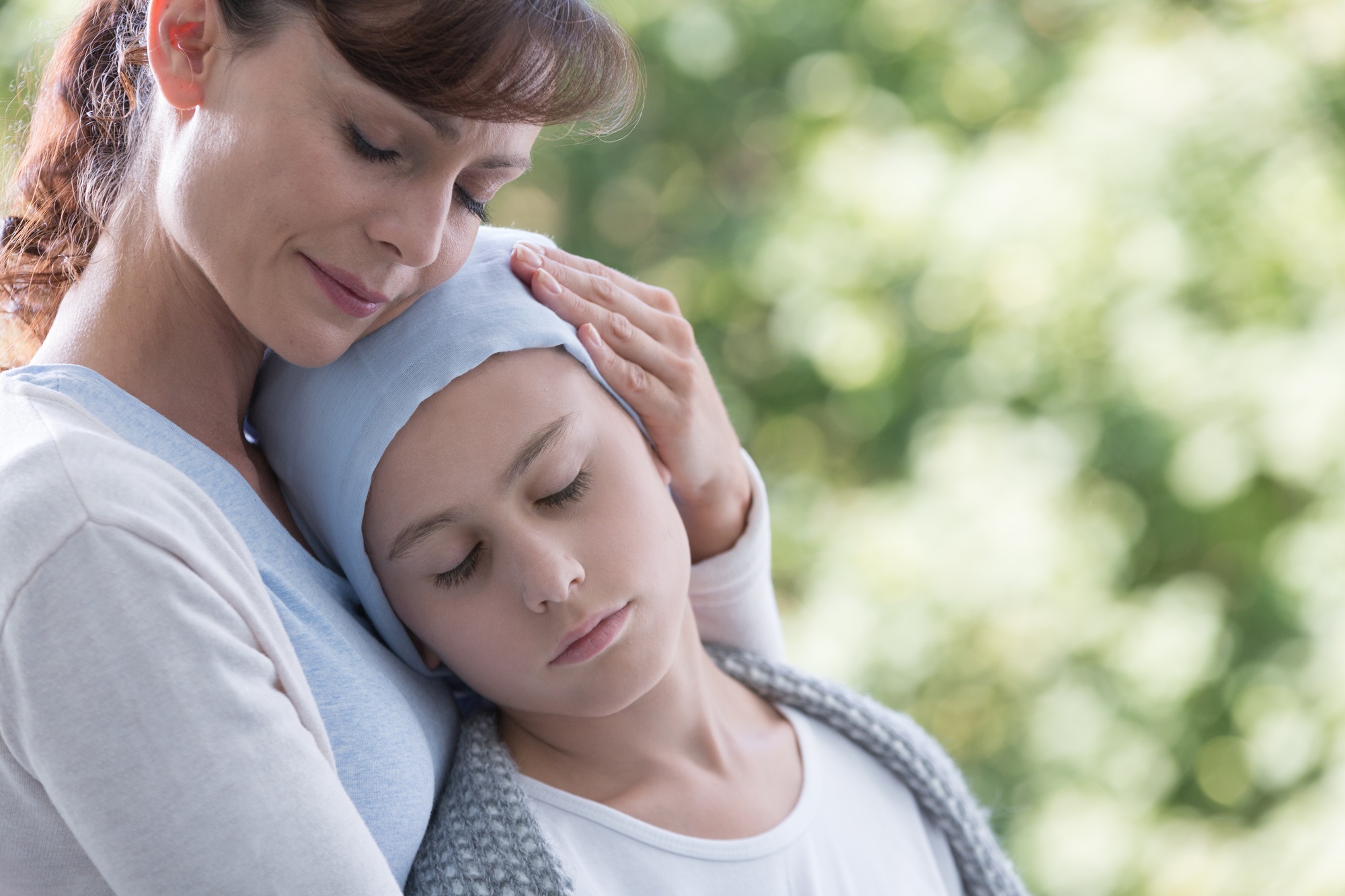 Caregiver hugging sick and weak kid with cancer during chemother